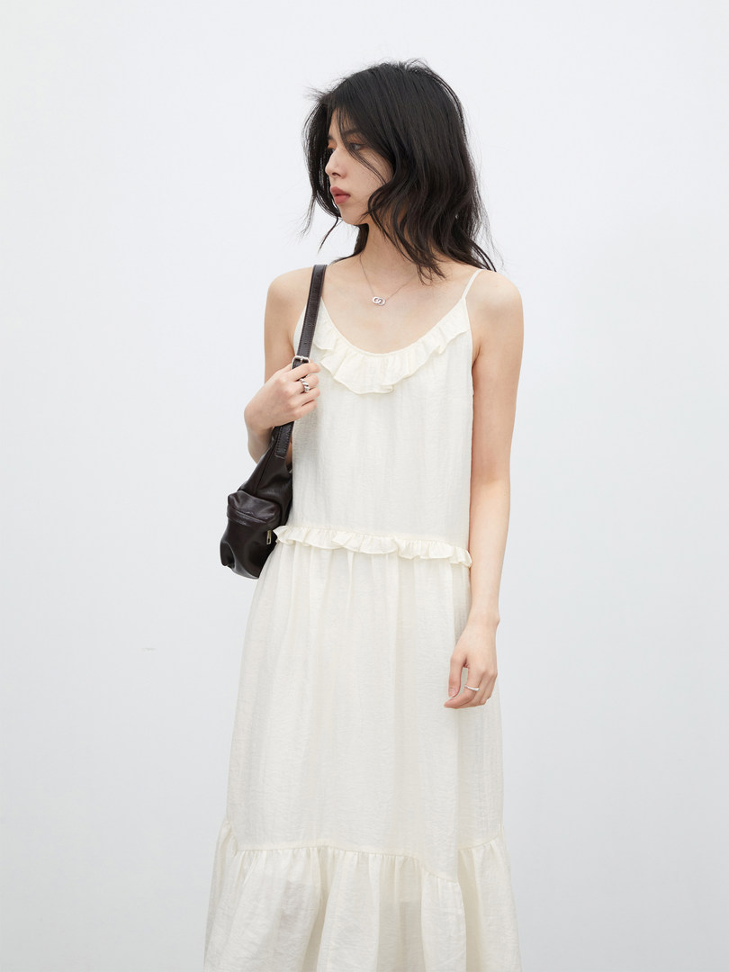 Model wearing a cream sleeveless ruffle dress with a black shoulder bag