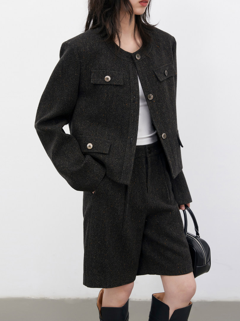 Model wearing a dark tailored jacket and matching shorts set with a black handbag
