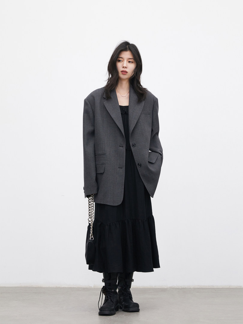Model wearing a dark gray oversized blazer over a black dress with black boots and a chain bag