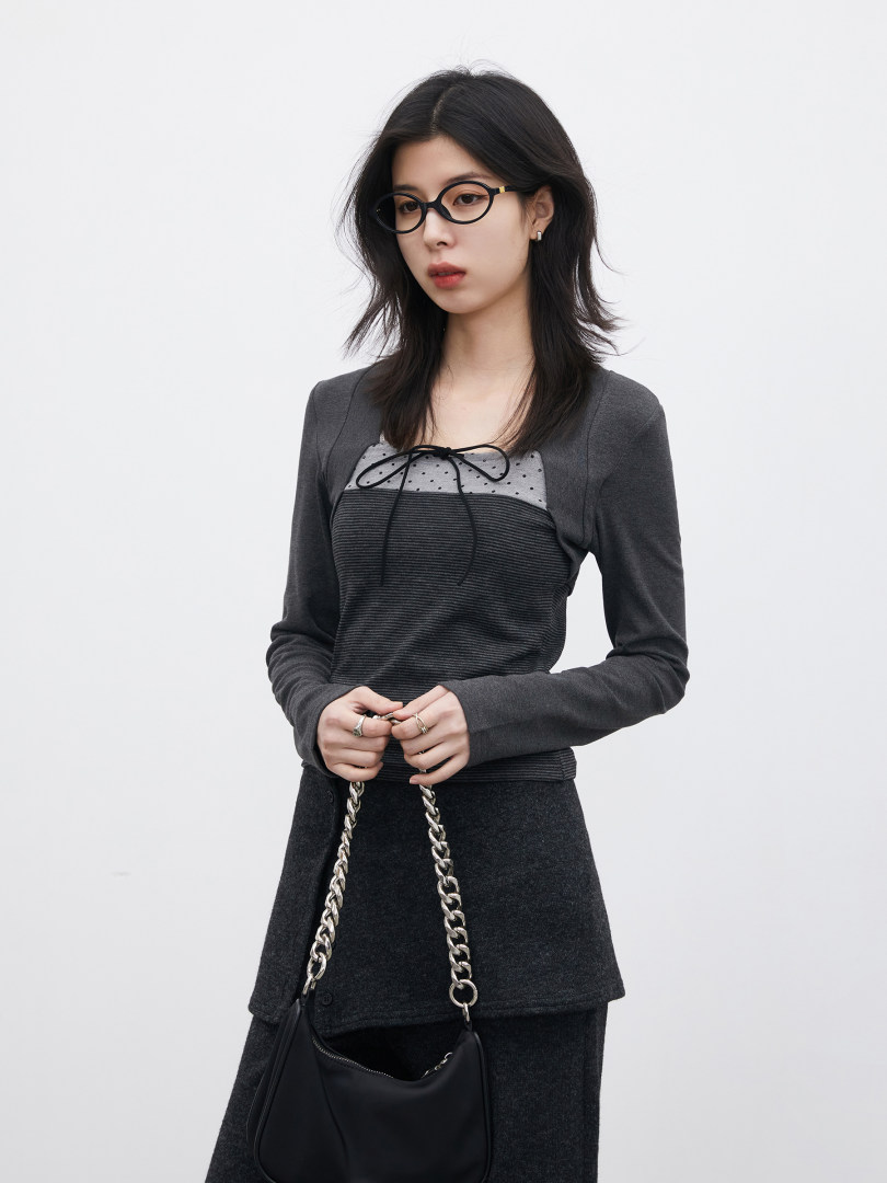 Model wearing a dark layered long-sleeve top and skirt with a chain-strap handbag