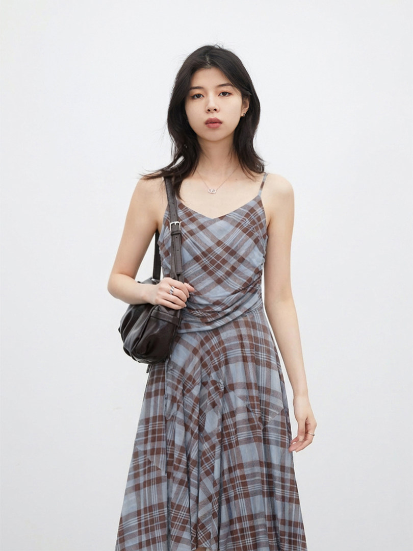 Model wearing a sleeveless plaid dress with a black shoulder bag on a plain background