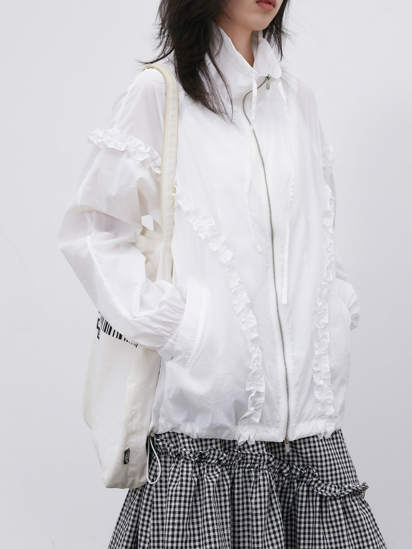 Model wearing a white ruffled zip-up jacket with a gingham skirt and tote bag