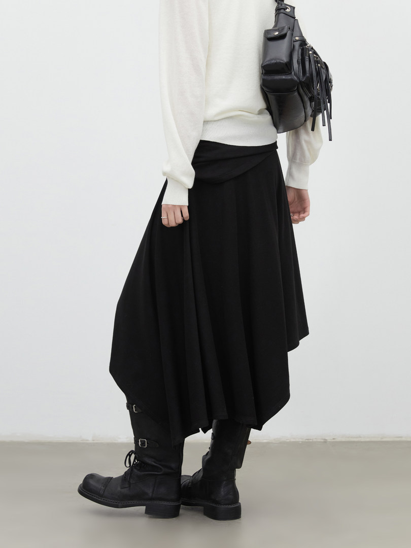 Model wearing a white sweater, black skirt, black boots, and a black shoulder bag