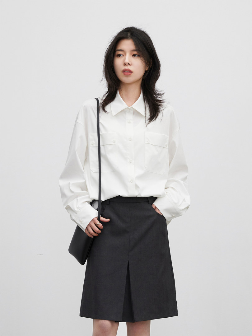 Woman wearing a white button-up shirt with a dark skirt and small black shoulder bag
