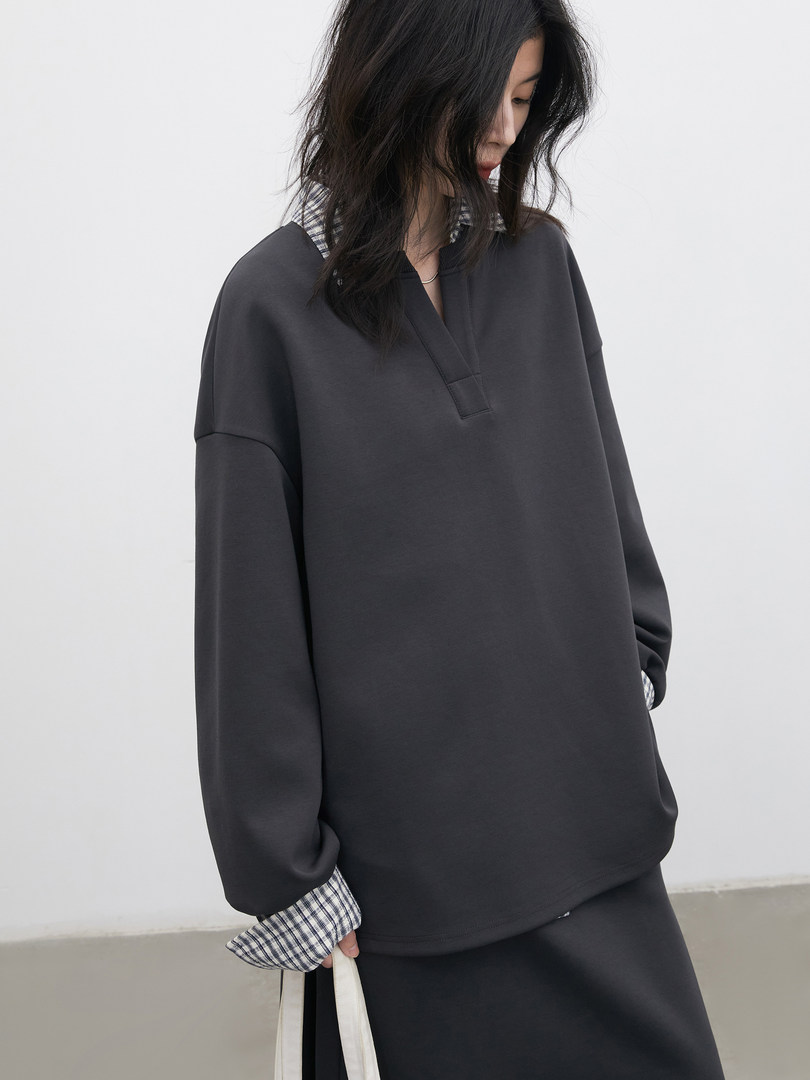 Model wearing an oversized dark long-sleeve top with plaid cuff details