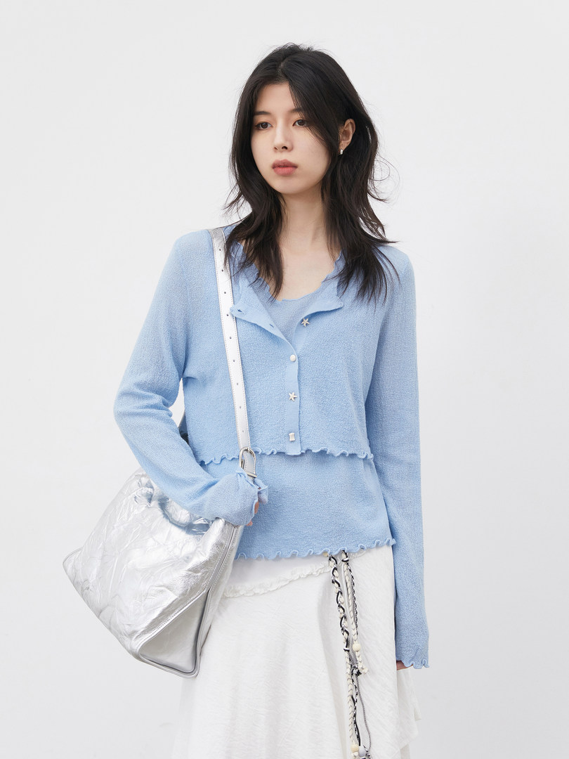 Model wearing a light blue textured cardigan with a white skirt and silver bag