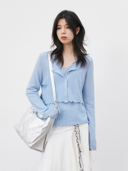 Model wearing a light blue textured cardigan with a white skirt and silver bag