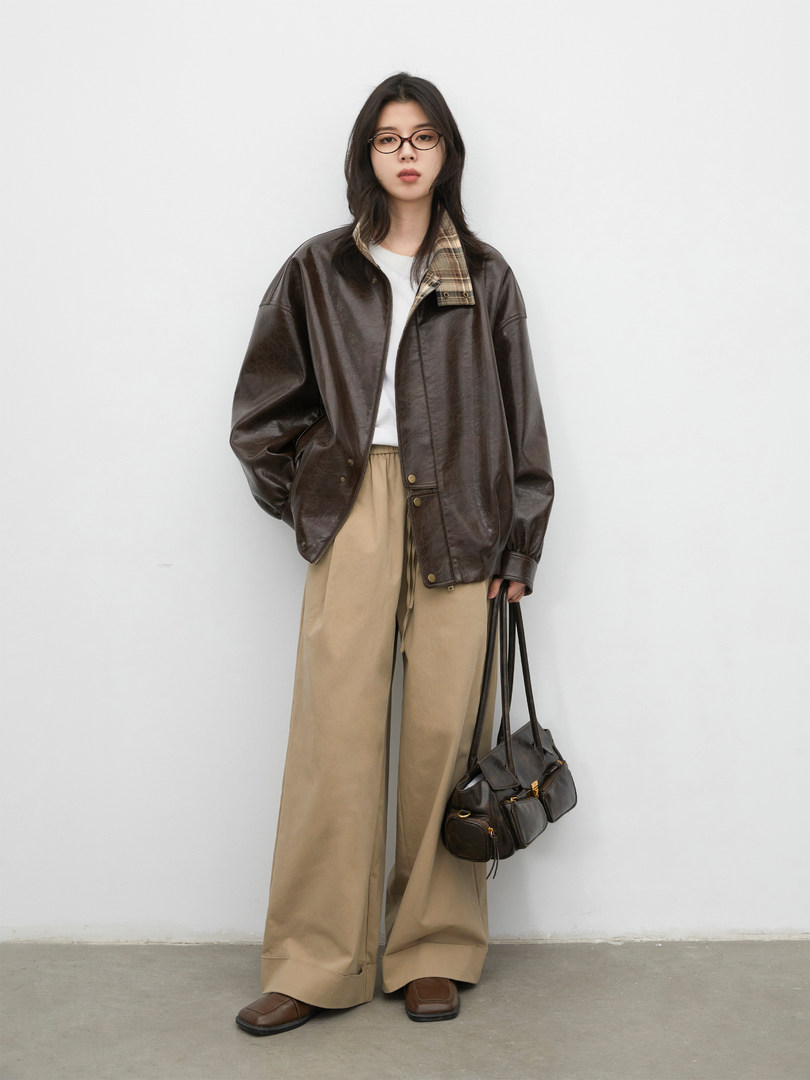 Model wearing a dark brown leather jacket with beige wide-leg trousers and a black shoulder bag