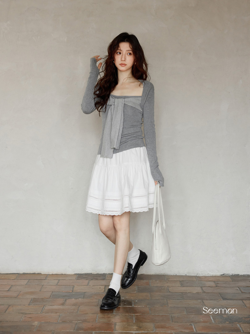 Woman modeling a gray long-sleeve top with a white skirt, black loafers, and a white shoulder bag