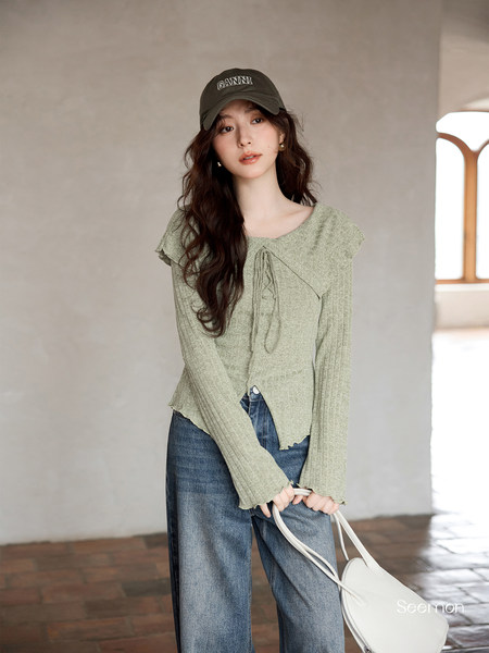 Model wearing a light green knit top with jeans and a cap