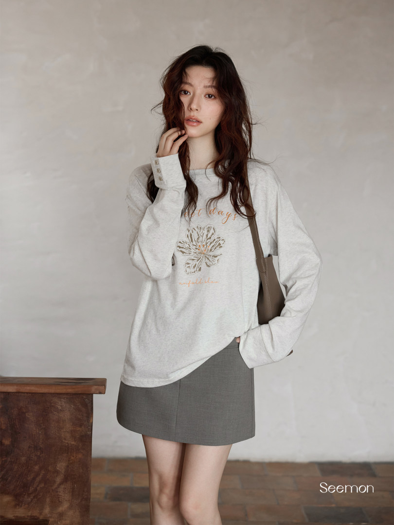 Model wearing a light gray graphic long-sleeve sweatshirt with a gray mini skirt
