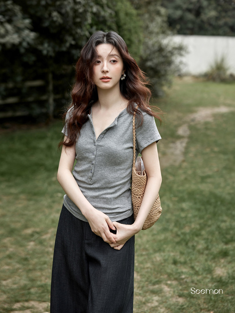 Woman wearing a gray short-sleeve button henley top with dark wide-leg pants and a woven shoulder bag