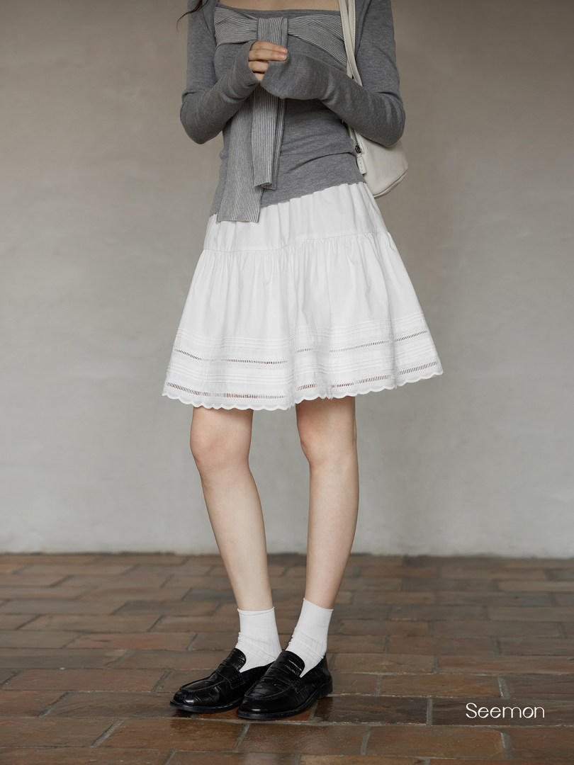 Woman wearing a gray knit top with a white tiered skirt and black loafers