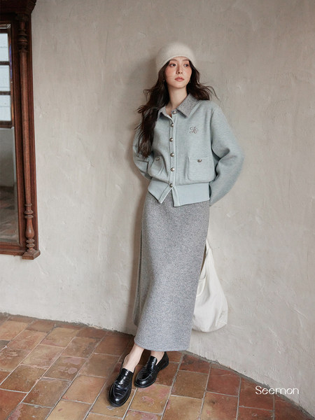 Woman modeling a light gray knit jacket and matching skirt with a white beanie and black loafers