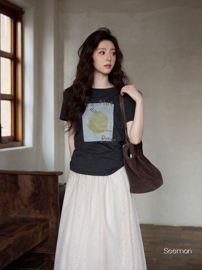 Model wearing a black graphic T-shirt with a white long skirt and brown shoulder bag