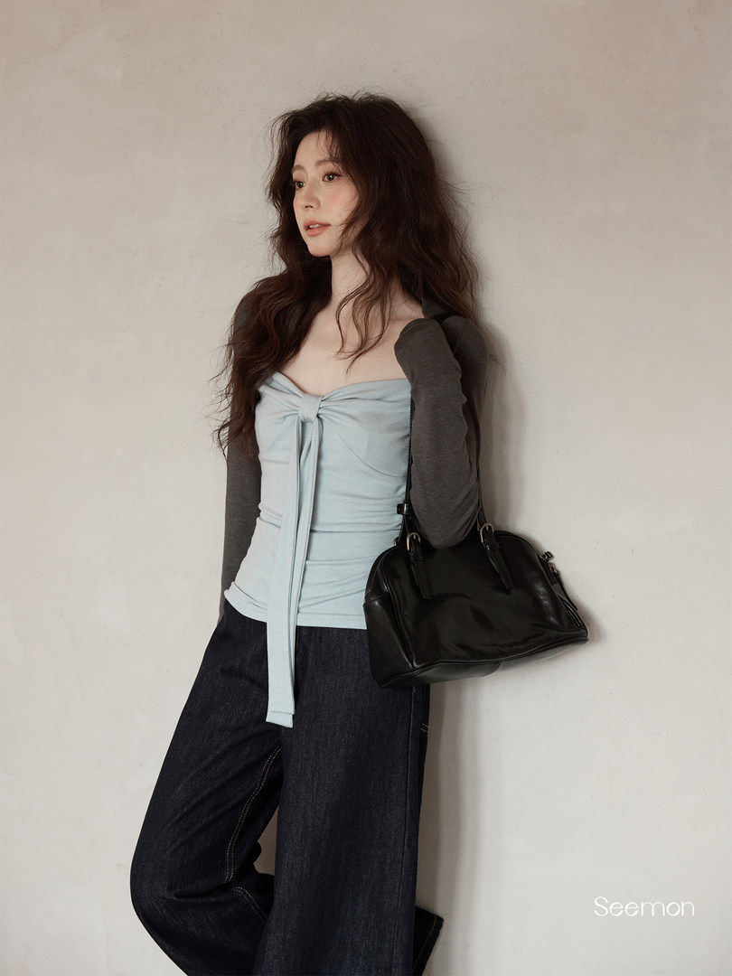Model wearing a light blue strapless top with dark wide-leg jeans and a black handbag