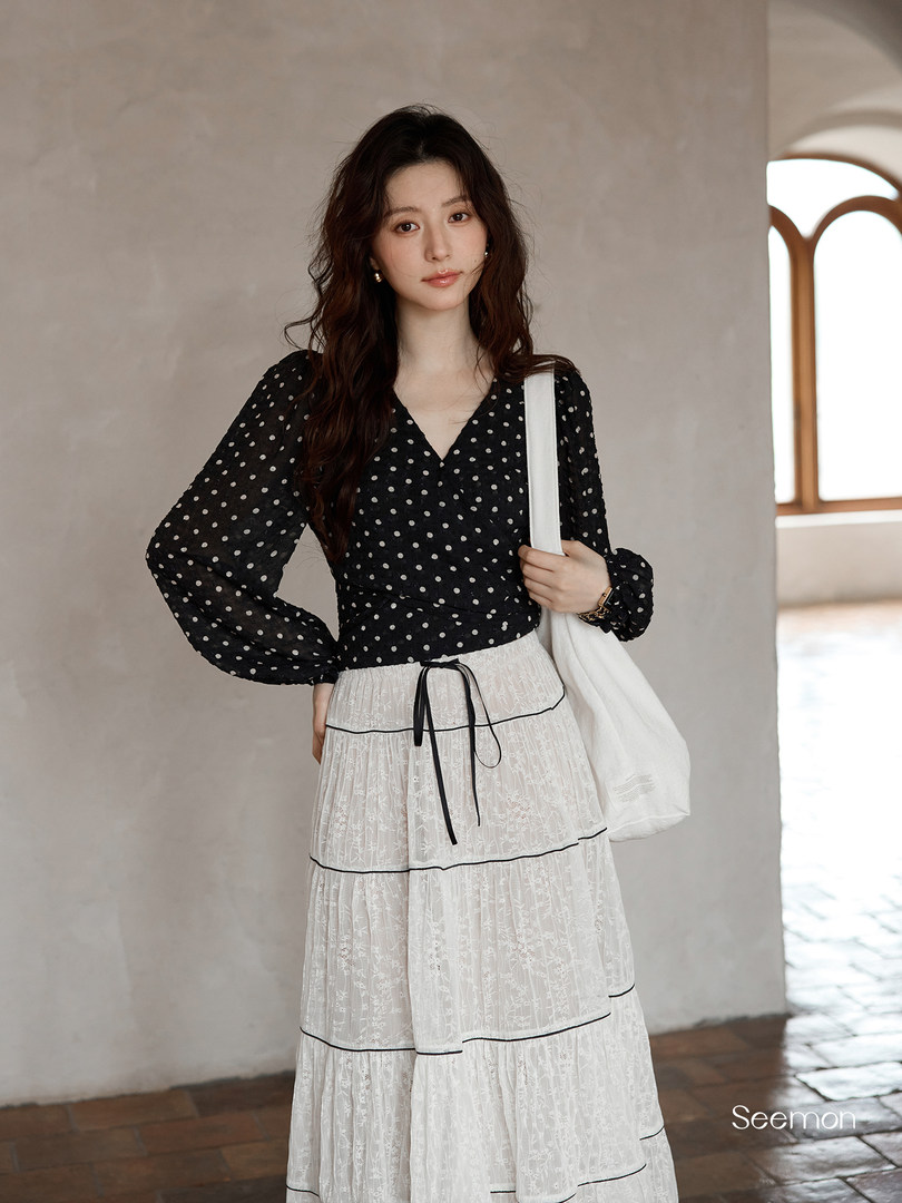 Woman wearing a black polka dot blouse with a white lace tiered skirt and white shoulder bag