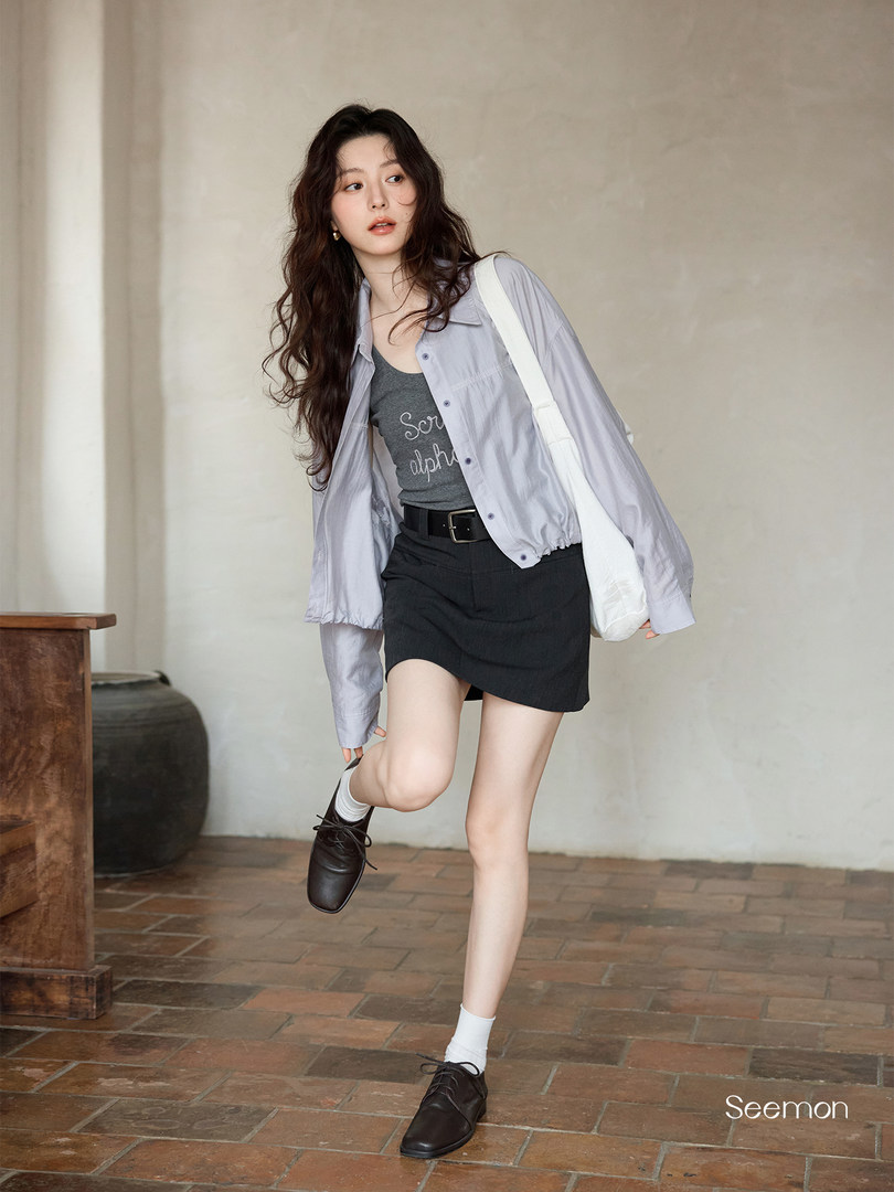 Model wearing a light gray shirt over a dark tank top with a black skirt and black shoes
