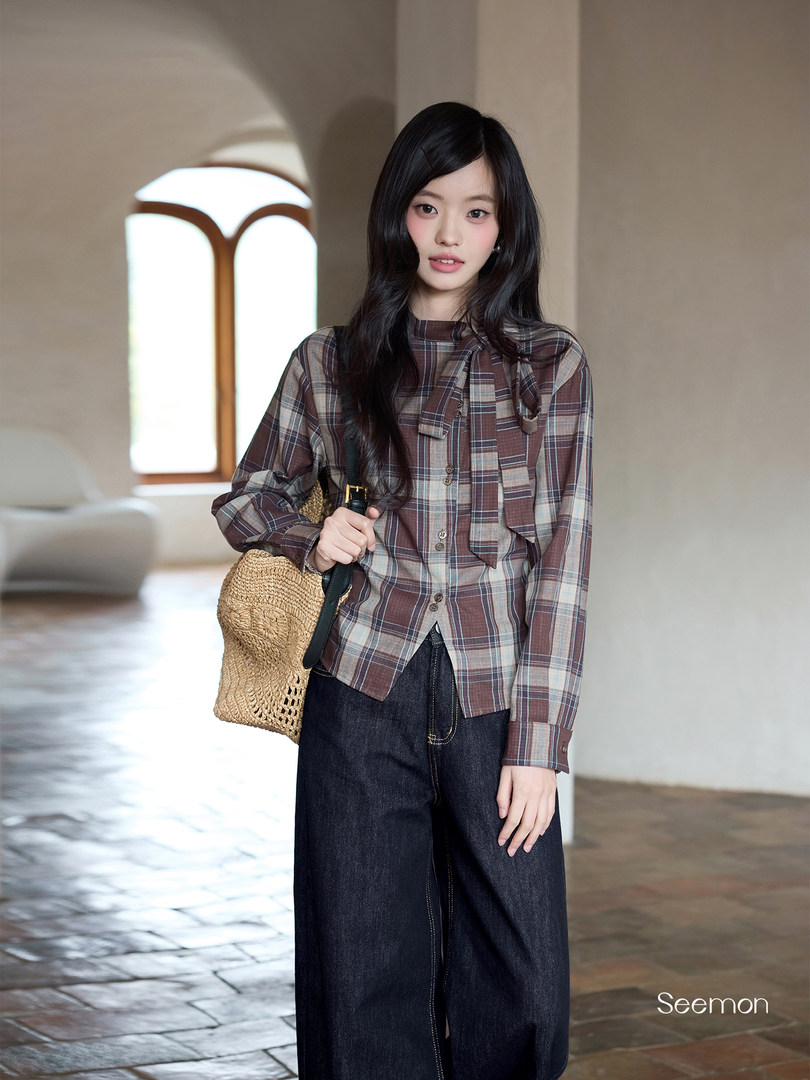 Model wearing a brown plaid long-sleeve blouse with dark wide-leg jeans and a woven shoulder bag