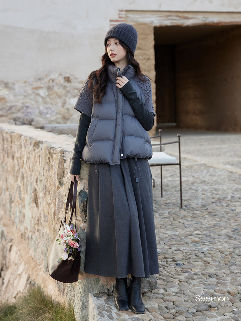Model wearing a dark gray puffer vest and long skirt with beanie and boots
