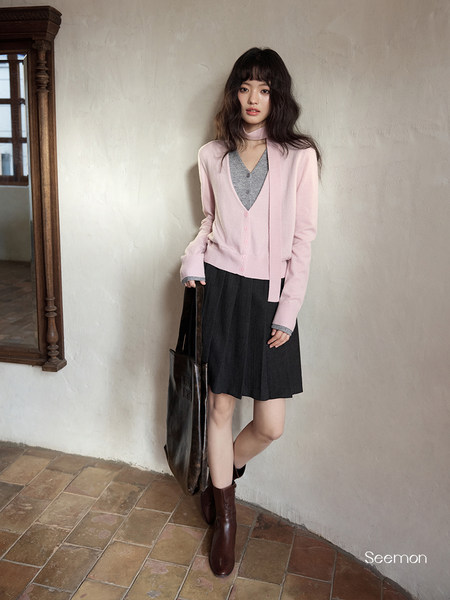 Woman wearing a pink cardigan, gray top, black skirt, and brown boots