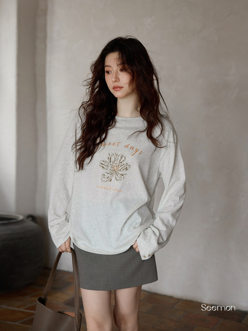 Model wearing a light gray long-sleeve sweatshirt with floral graphic and gray mini skirt