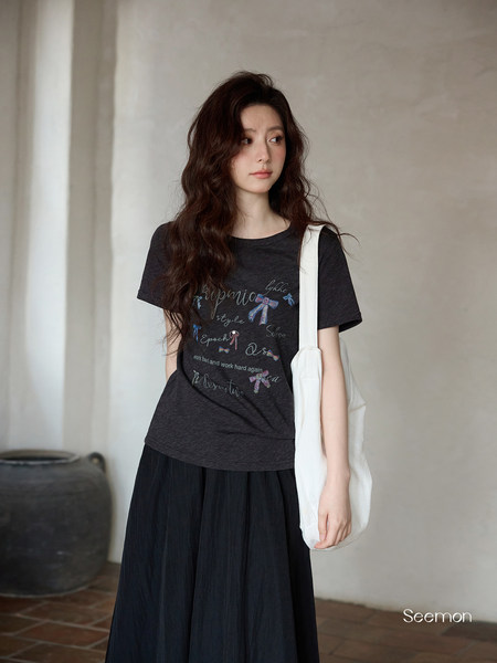 Model wearing a black graphic short-sleeve T-shirt with a white tote bag and long black skirt