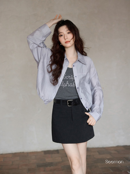 Woman modeling a light blue button-up shirt with a black mini skirt and belt