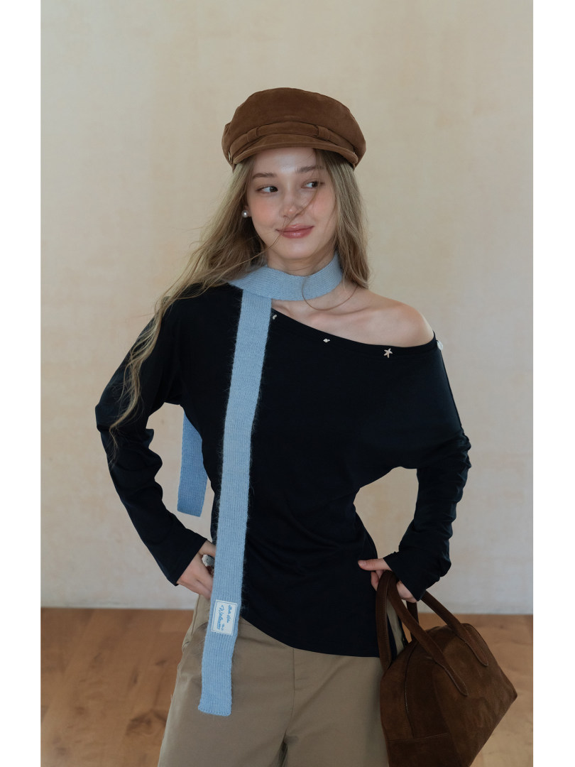 Woman modeling a black off-shoulder top with a blue scarf, brown hat, and handbag