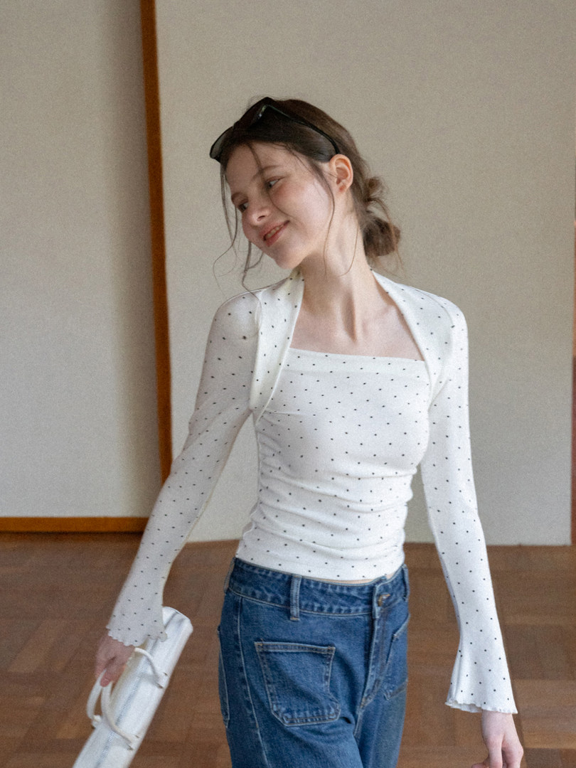 Model wearing a white polka dot long-sleeve fitted top with flared sleeves and blue jeans