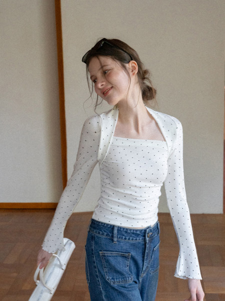 Model wearing a white polka dot long-sleeve fitted top with flared sleeves and blue jeans