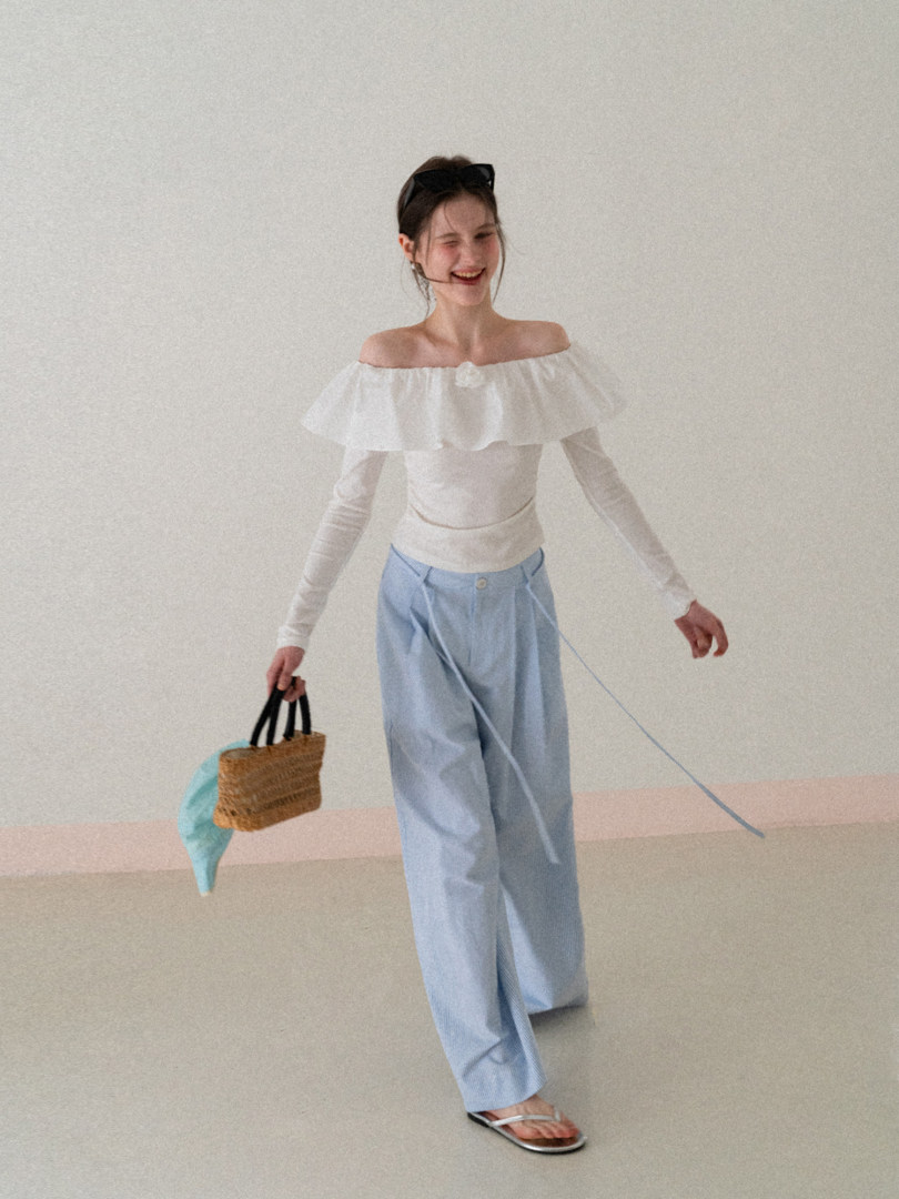 Model wearing a white off-shoulder top with light blue wide-leg pants and a straw handbag