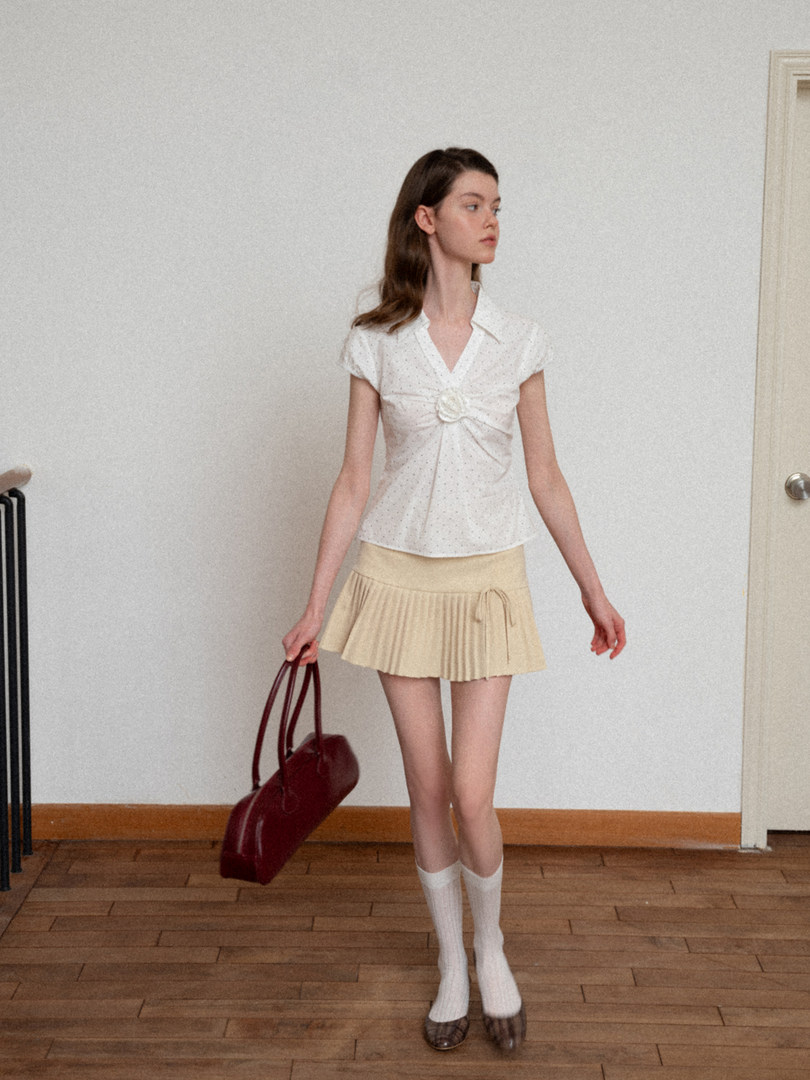 Model wearing a white short-sleeve top and pale pleated mini skirt with socks and loafers, holding a burgundy bag