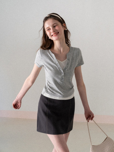 Model wearing a gray short-sleeve buttoned henley top with a dark skirt