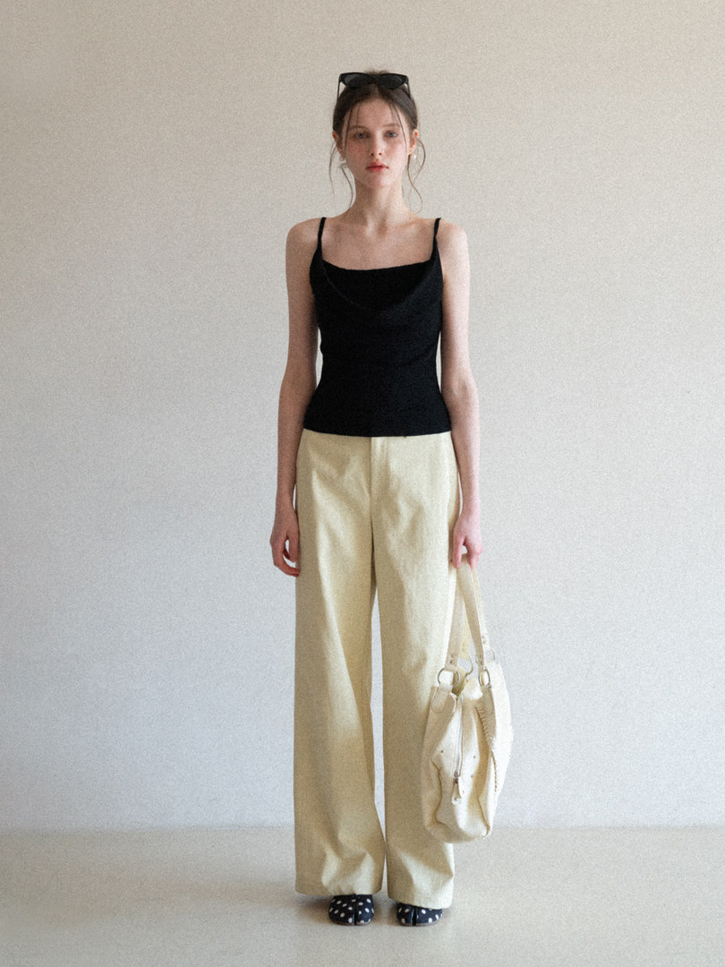 Model wearing a black camisole top with cream wide-leg pants and a white shoulder bag.