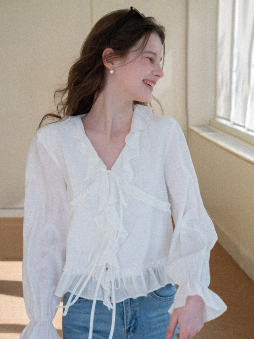 Woman wearing a white sheer ruffled blouse with long sleeves