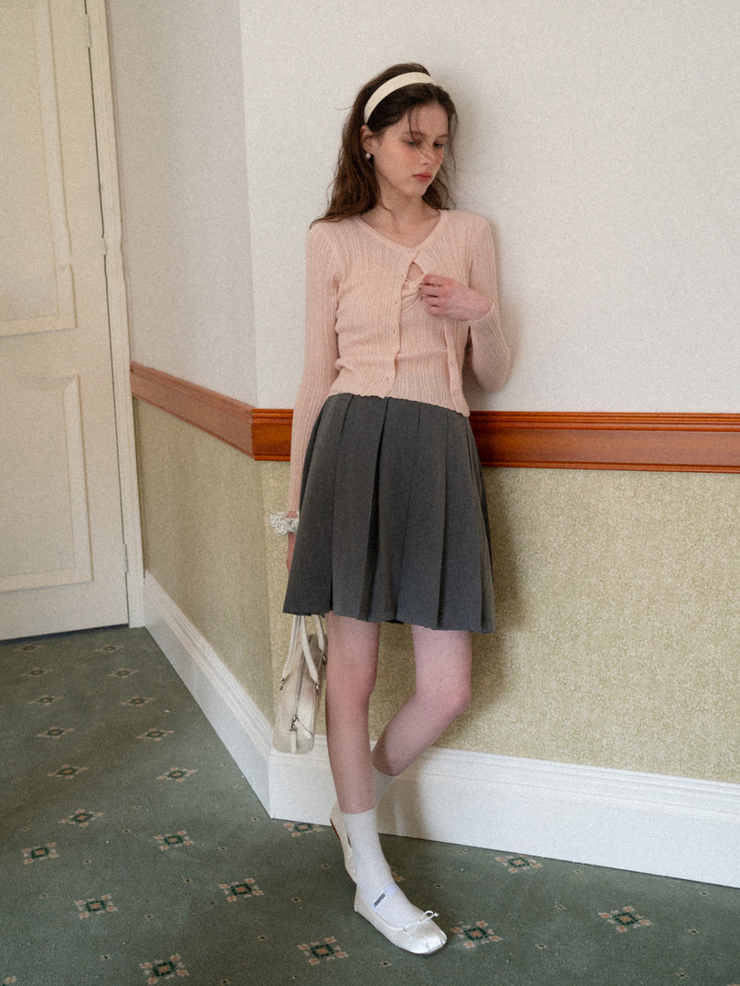 Model wearing a pale pink cardigan with a gray pleated skirt