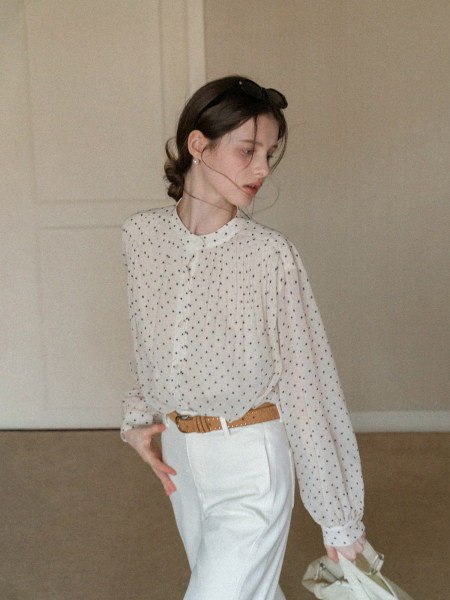 Model wearing a white polka dot long-sleeve blouse with white trousers and a brown belt