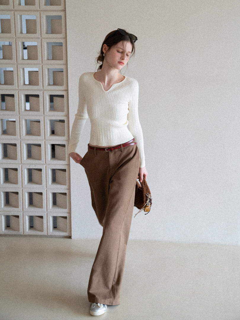 Woman wearing a cream knit long-sleeve top with brown trousers and a small handbag