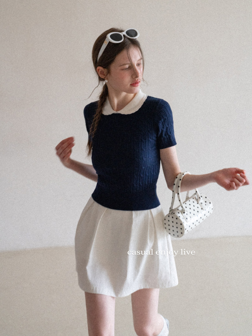 Model wearing a navy short-sleeve top with a white skirt and polka dot handbag