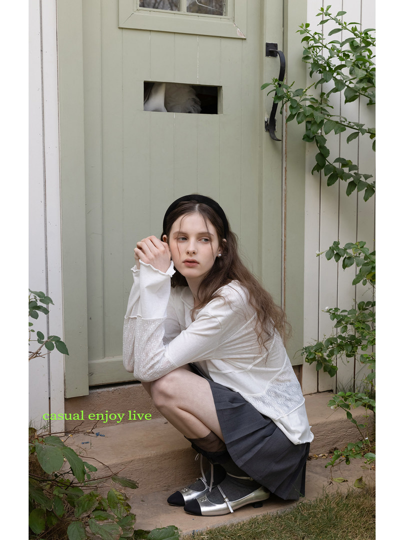 Model wearing a white long-sleeve top with lace sleeves, dark skirt, and silver flats outdoors.