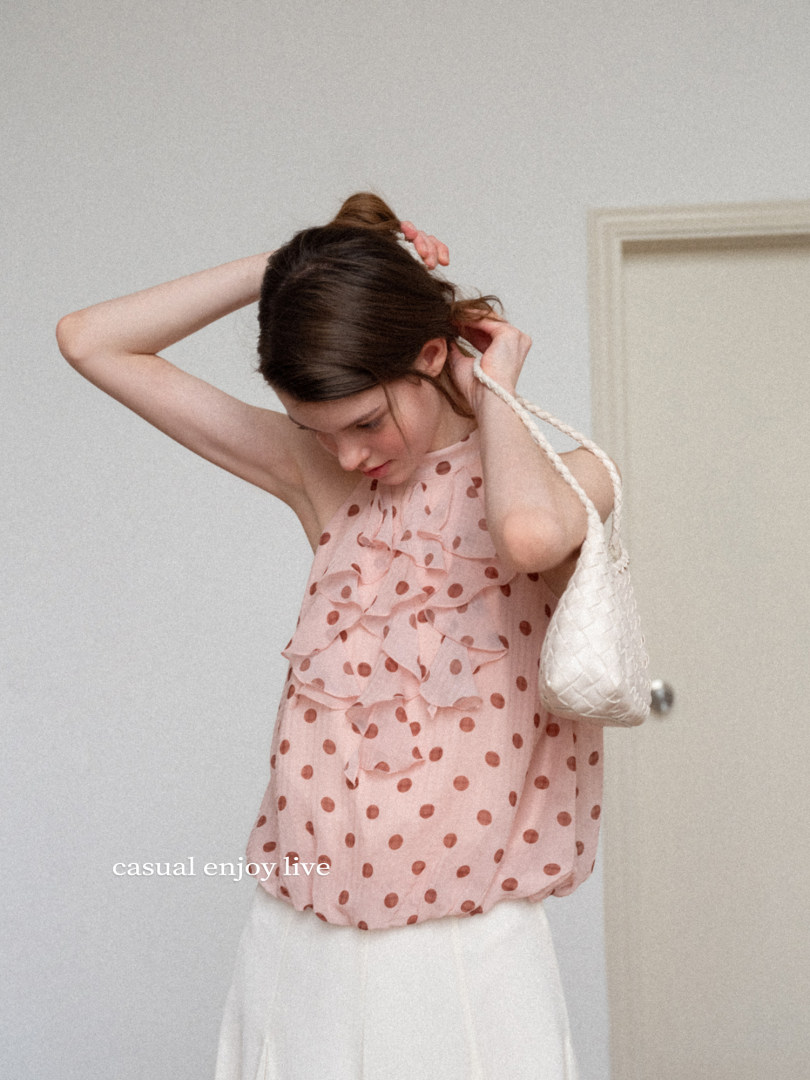 Woman wearing a pink polka dot ruffled sleeveless top with a white bag