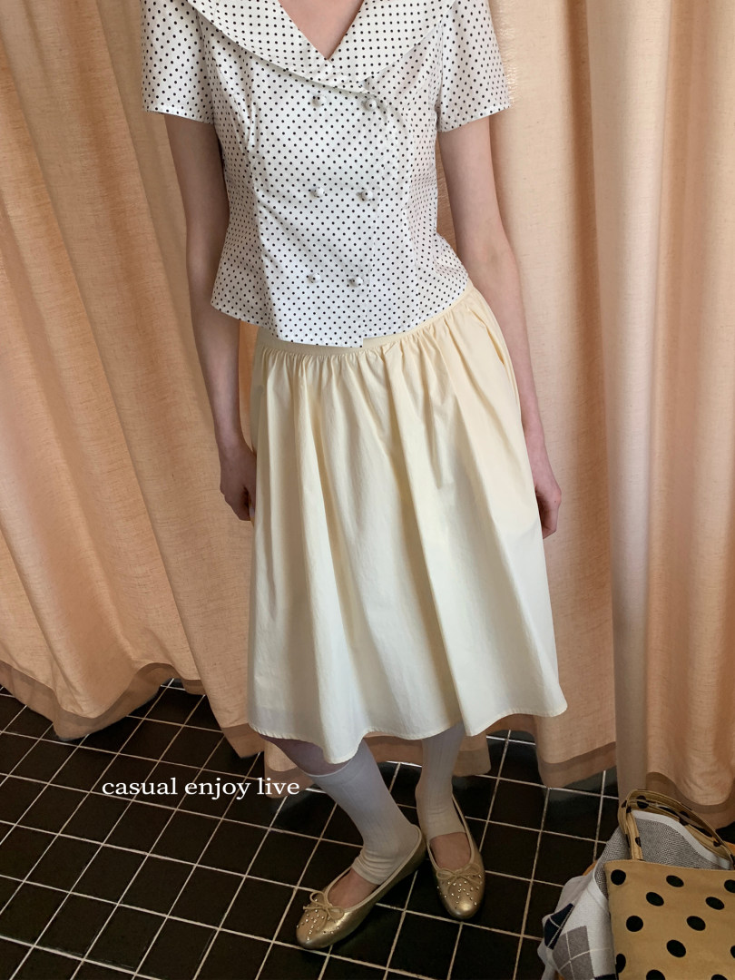 Model wearing a white polka dot blouse with a cream skirt and gold flats