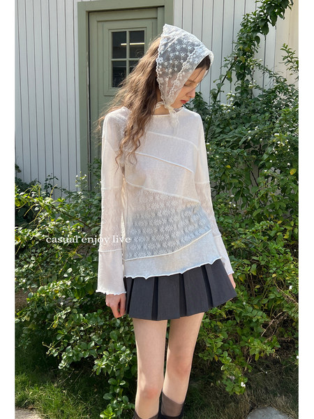 Model wearing a sheer white lace long-sleeve top with a dark pleated mini skirt outdoors