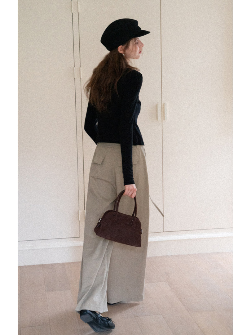 Model wearing a black long-sleeve top with beige wide-leg pants, a black cap, and a dark handbag