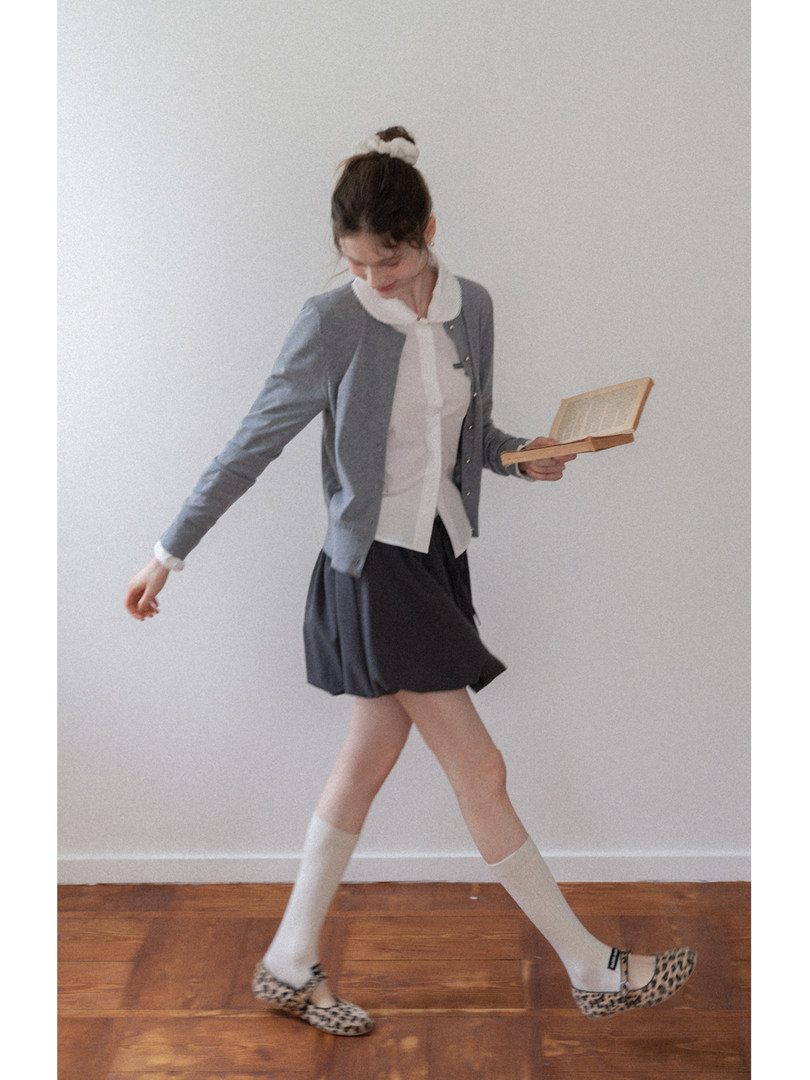 Model wearing a gray cardigan, white blouse, dark skirt, socks, and leopard flats