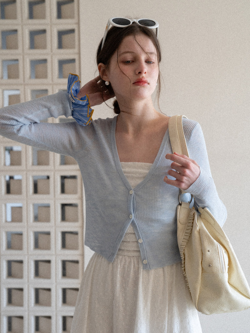 Woman wearing a light blue buttoned cardigan with a cream dress and beige shoulder bag