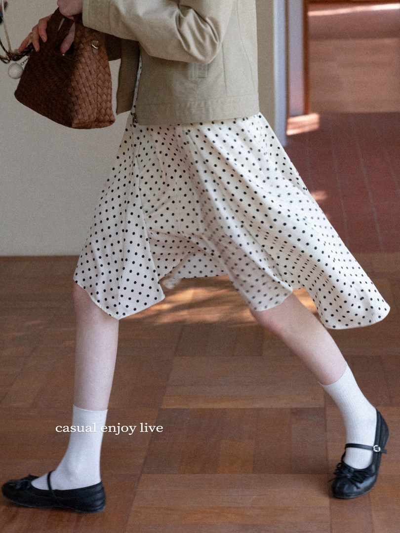 Model wearing a white polka dot skirt with black shoes and a brown woven handbag