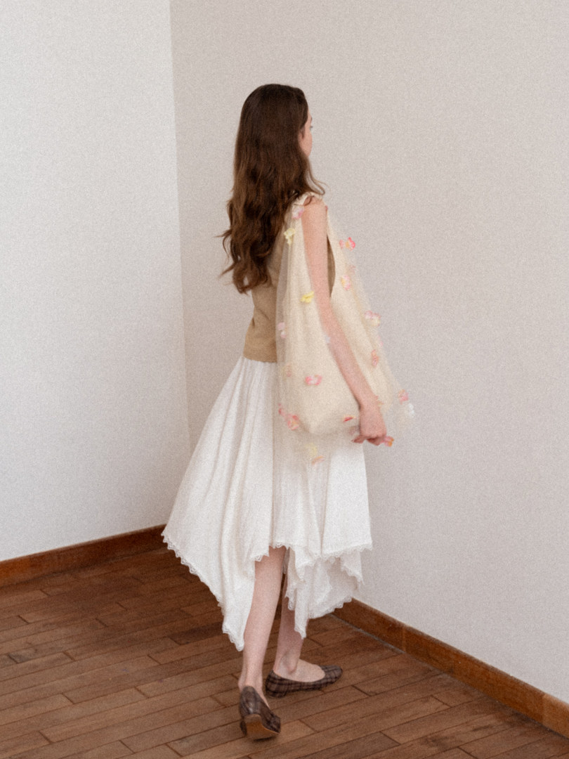Woman modeling a white flowy asymmetrical dress with a beige top and tote bag