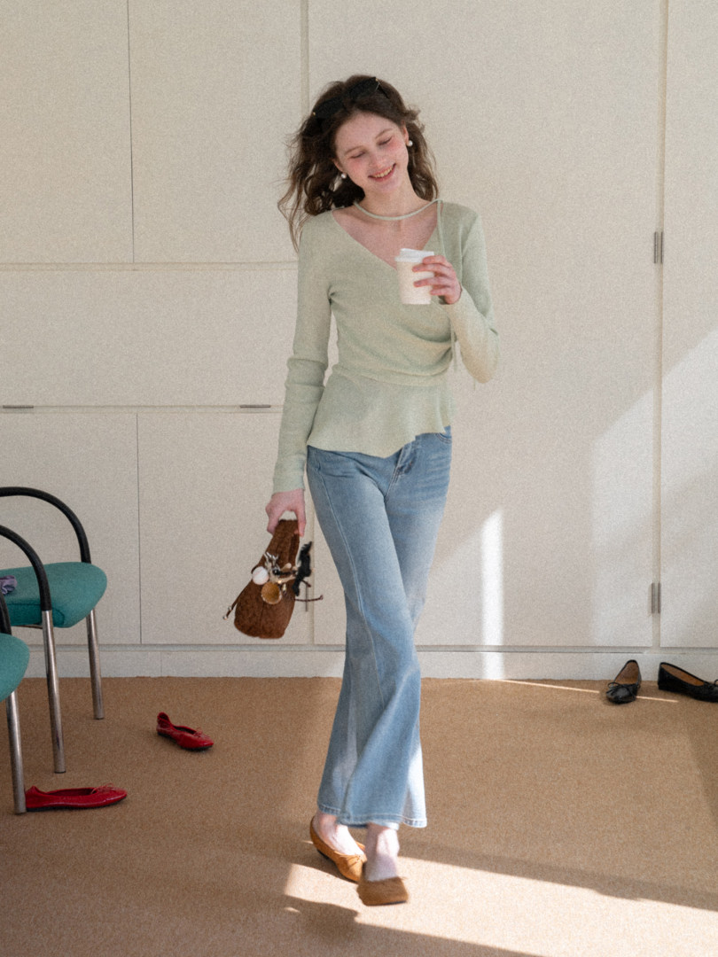 Woman wearing a light green wrap top with blue jeans and holding a small brown handbag